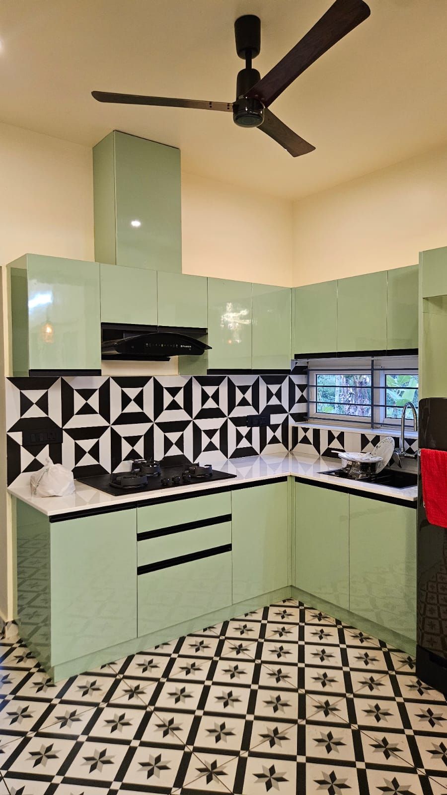 Modern kitchen design featuring glossy mint-green handleless cabinetry contrasted by a bold black-and-white geometric backsplash and patterned floor tiles.