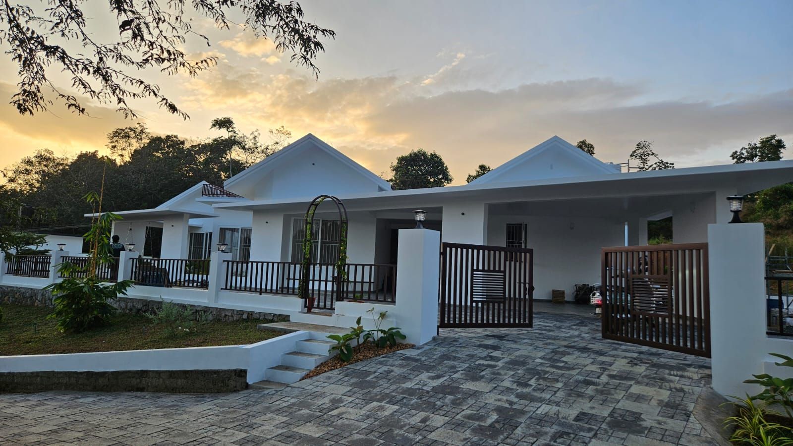 The residential project's front entrance at dusk, showing the main gate, carport, and illuminated gabled roofline.