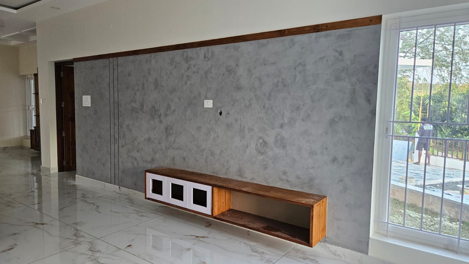 Modern living room interior with a grey textured accent wall, floating wooden TV console, and white marble-finish flooring.