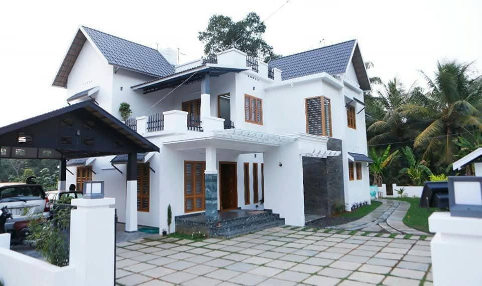 Daytime exterior shot of the modern home with a white facade, dark gabled roofs, and a paved driveway.
